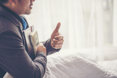 Midsection of businessman holding money and document while showing thumbs up on bed