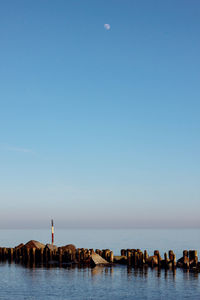 Rocks and wooden posts in sea against clear blue sky