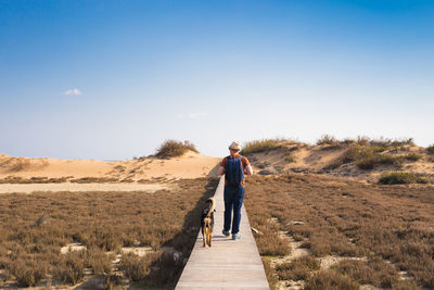 Men walking on dirt road amidst land against sky