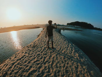 Rear view of man photographing at beach against sky during sunset