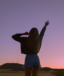 Rear view of woman standing against clear sky during sunset