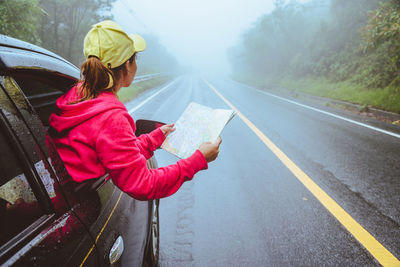 Rear view of woman holding umbrella on road during rainy season