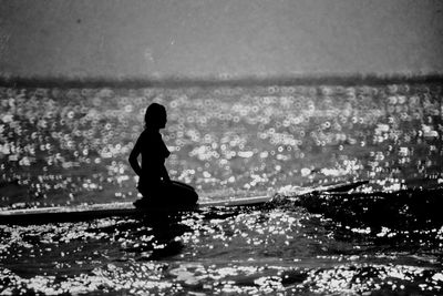 Silhouette woman kneeling over surfboard on sea