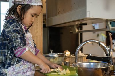 Side view of girl chopping vegetable at kitchen