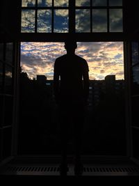 Silhouette man standing by window at sunset