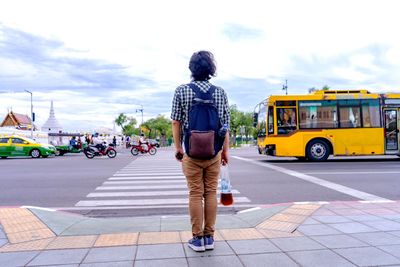 Rear view of man standing on street in city against sky