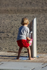 Full length rear view of boy filling water in bucket at beach