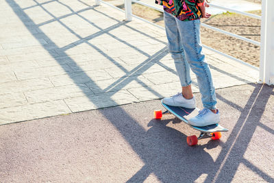 Unrecognizable stylish skater in jeans and sneakers standing on skateboard in skatepark on sunny day in summer