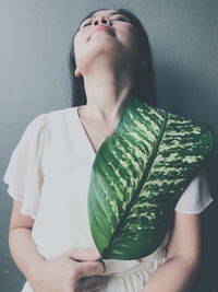 Young woman with green leaf standing against wall