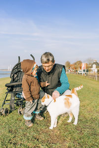 Grandfather and granddaughter stroking cat on field against sky