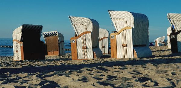 Hooded chairs on beach against clear blue sky