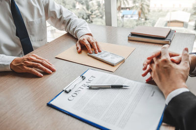 Midsection of real estate agent giving key to client in office