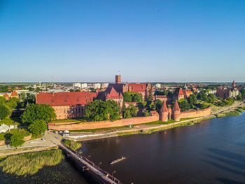 Bridge over river by buildings against clear blue sky