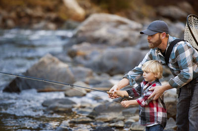 Father fishing with son by river at forest