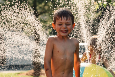 Water splashing on shirtless boy standing in yard