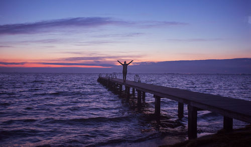 Silhouette person standing by sea against sky during sunset