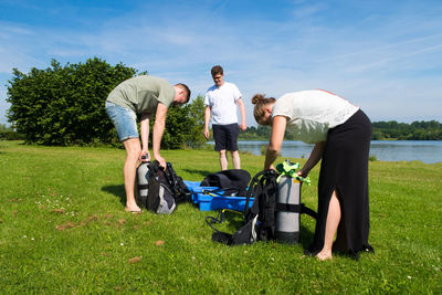 Scuba divers preparing their equipment by lake against sky