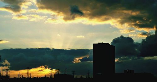 Silhouette factory against sky during sunset