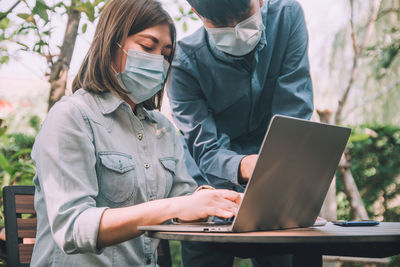 Portrait of business people wearing mask using looking at laptop outdoors