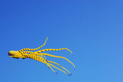 Low angle view of yellow flying against clear blue sky