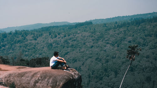 Man sitting on rock against mountains