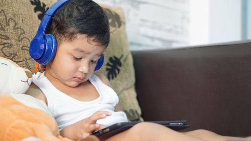 Boy using mobile phone while sitting on bed at home