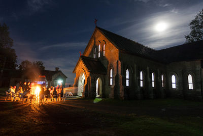 People in illuminated building against sky at night