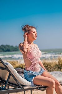 Young woman sitting on deck chair against sky