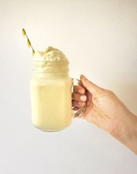 Close-up of hand holding drink against white wall