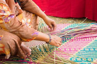 Low section of woman making wicker mat