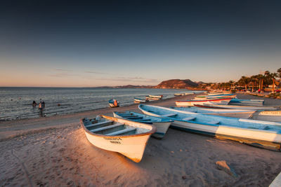 Rowboats moored at beach against sky during sunset