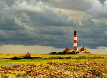 Lighthouse on field by building against sky