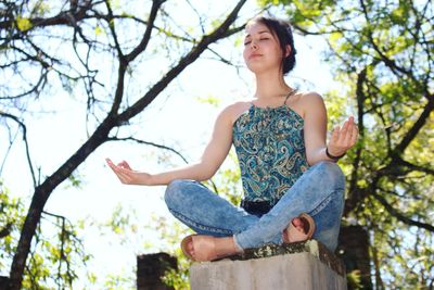 Low angle view of teenage girl meditating against sky