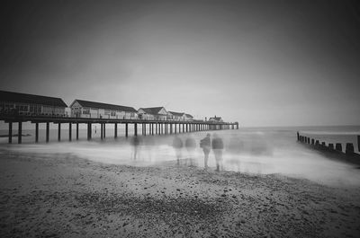 Multiple exposure of man standing at sea by pier against cloudy sky