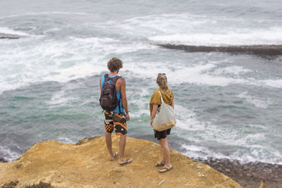 High angle view of couple standing on rock while looking at sea