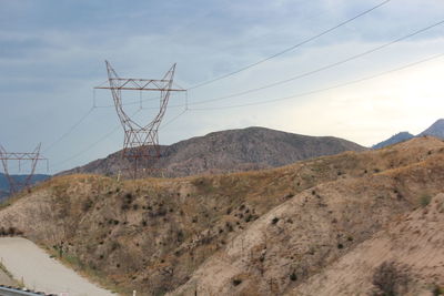Electricity pylon by mountains against sky