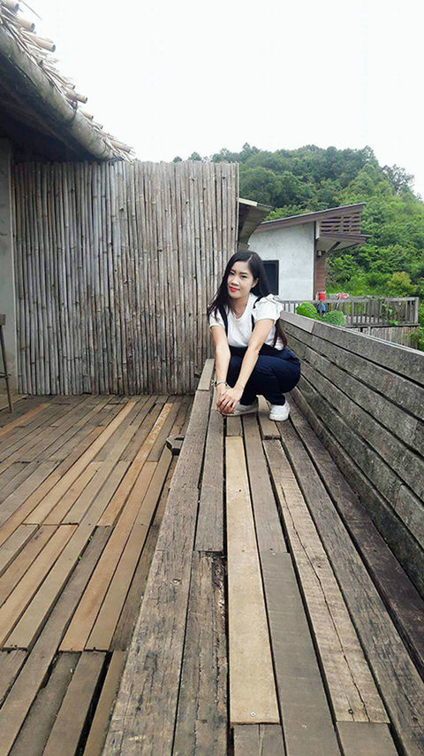 wood - material, sitting, full length, young adult, outdoors, young women, one person, day, built structure, real people, lifestyles, women, clear sky, relaxation, looking at camera, sky, wood paneling, portrait, tree, architecture, building exterior, nature, adult, people