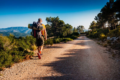 Rear view of man with backpack walking on dirt road