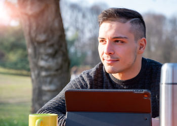 Smiling freelancer with tablet pc sitting in park on sunny day