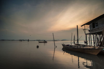 Boats moored by stilt house in river at sunset