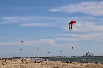 People enjoying at beach against sky during sunset