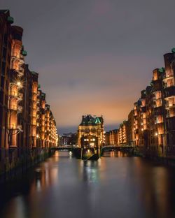 Illuminated buildings by river against sky at night