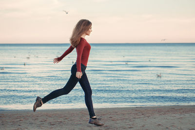 Full length of woman running at beach against sky