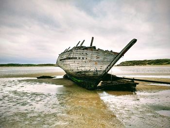 Abandoned boat on beach against sky