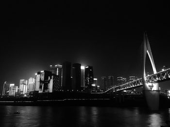 Illuminated bridge over river in city against clear sky at night