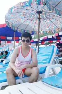 Portrait of man wearing sunglasses while sitting on lounge chair at beach