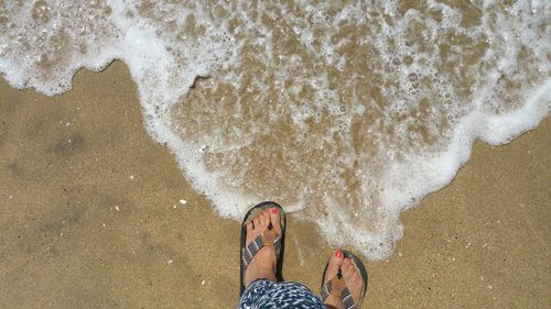 Low section of person feet in flip flops and water standing on beach