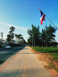 Road by footpath in city against sky