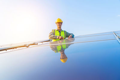 Portrait of male engineer repairing solar panels against blue sky