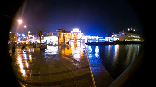 Boats moored on illuminated city by sea against sky at night